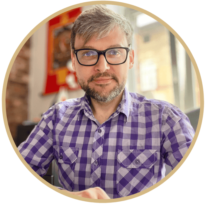 Piotr Dacjusz Górski w biurze, uśmiechnięty, w okularach i koszuli w kratę.